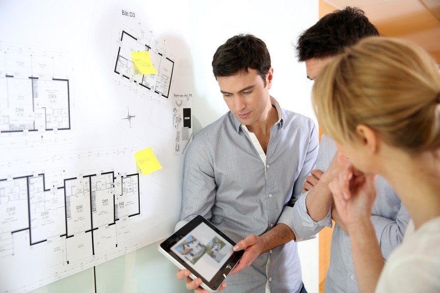 a man holding an ipad in front of two people while standing in front of architectural drawings.