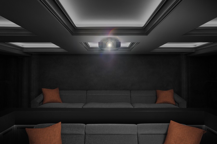 A luxury home cinema setup with a ceiling-mounted projector, recessed lighting, and dark-toned home theater seats with orange cushions